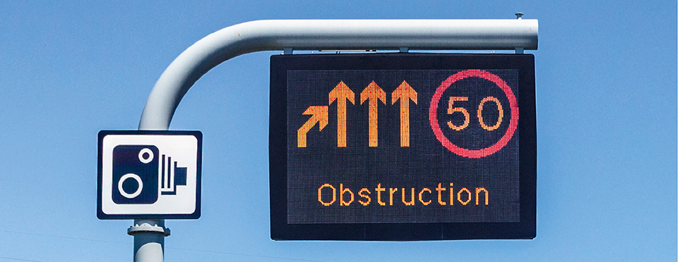 Overhead motorway gantry sign showing amber arrows directing traffic to the right with a red 50 mph limit and the word 'Obstruction'