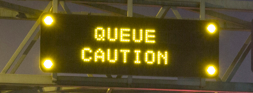 Amber matrix sign over the motorway showing the message 'QUEUE CAUTION'